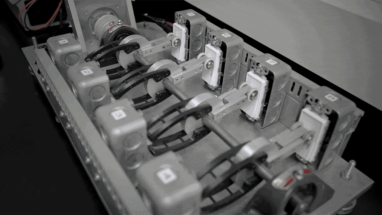 A switch test rig with four single-pole switches on one side and four rocker switch panels on the other separated by a motor that turns one side on while turning the other side off. 