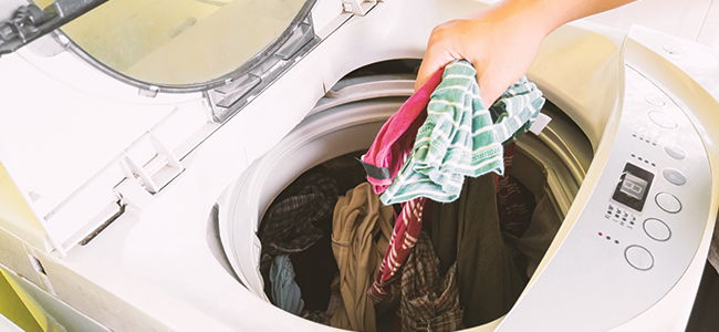 A hand puts clothing into a top-loading washing machine. 