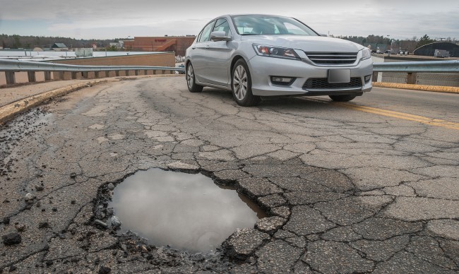 A car drives by a pothole down a paved road. 