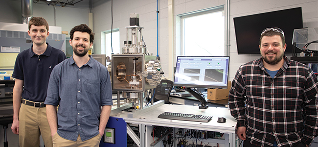  Patrick Drew, Nathan Pereira, and Mason Wood stand alongside the new Vacuum Bearing Test Rig at Nye Lubricants.